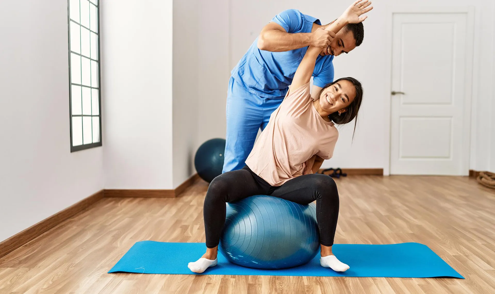 Bewegungstherapie im Reha-Zentrum Bad Hofgastein &ndash; Physiotherapeut unterst&uuml;tzt Patientin bei Dehn&uuml;bung auf Gymnastikball